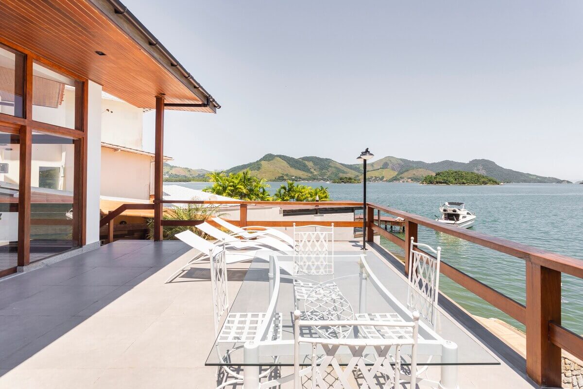 Deck privativo de madeira da Casa Kaîre estendendo-se sobre o mar calmo de Angra dos Reis, perfeito para relaxamento e atividades náuticas como stand-up paddle.