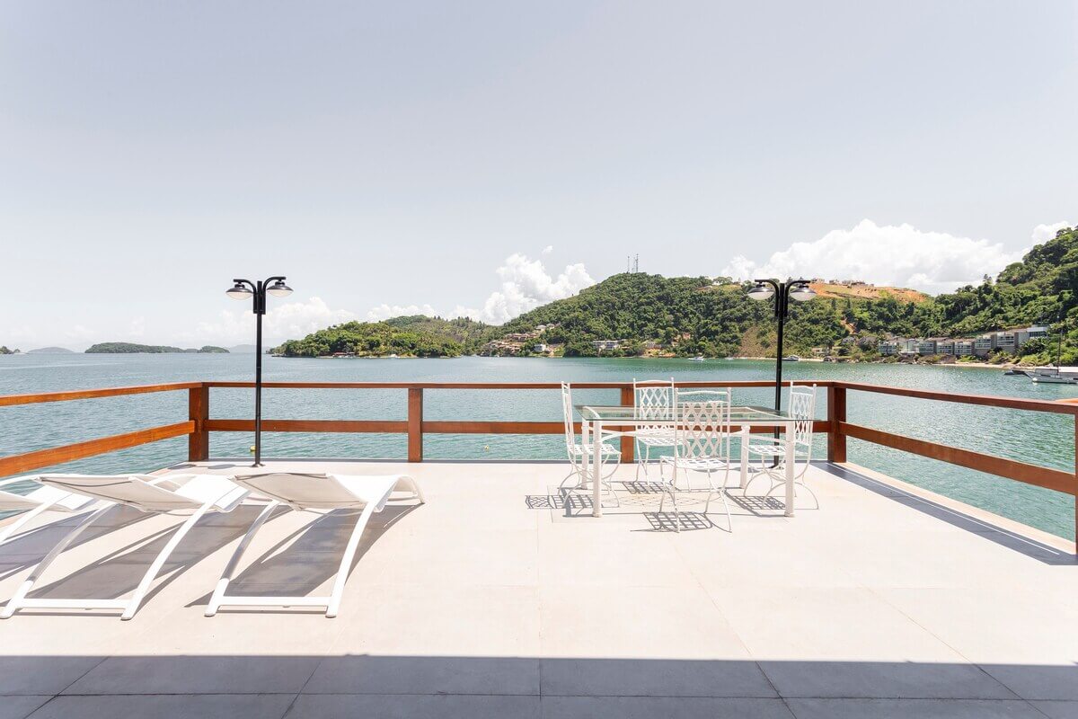 Vista panorâmica da Casa Kaîre em Angra dos Reis, destacando a arquitetura integrada à natureza, deck privativo sobre águas calmas e o cenário paradisíaco da Costa Verde.